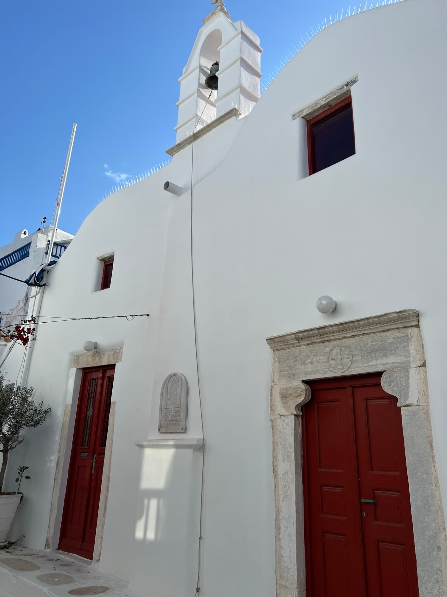 Whitewashed church with red doors and a bell tower in Mykonos