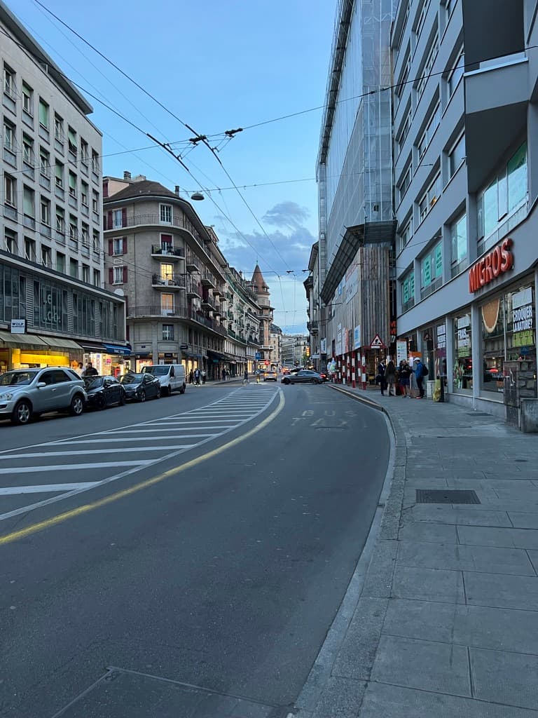 A street at dusk near a Migros storefront in Geneva